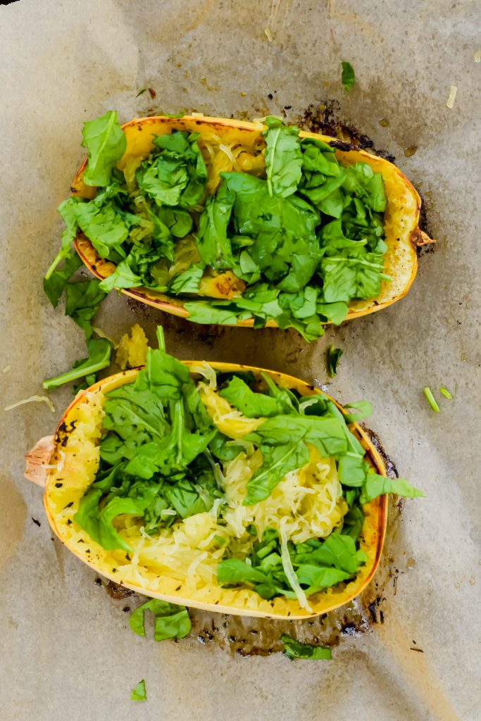 Halved baked spaghetti squash filled with greens on parchment paper