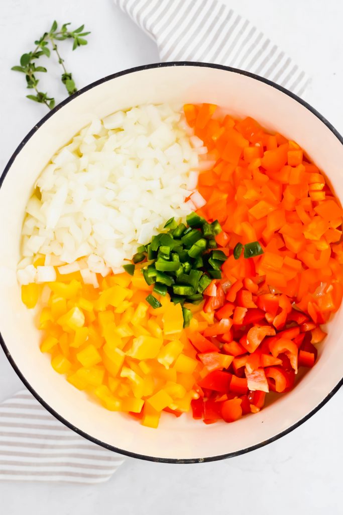 Large pot filled with separated portions of carrots, peppers and onions on striped linen backdrop