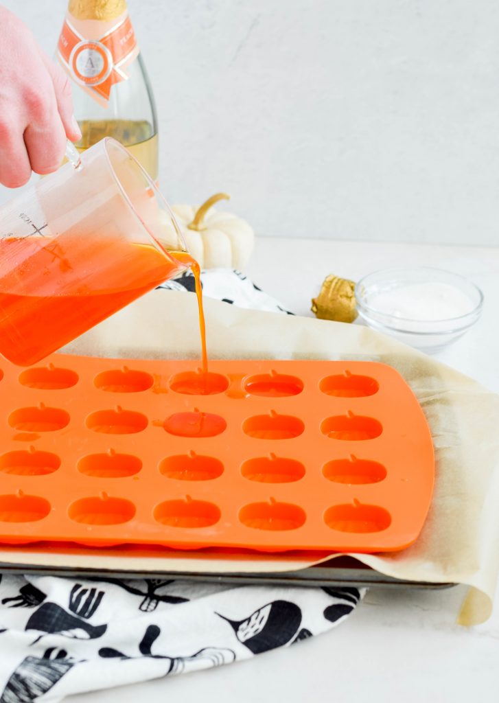 hand pouring liquid jello mixture into pumpkin silicon molds