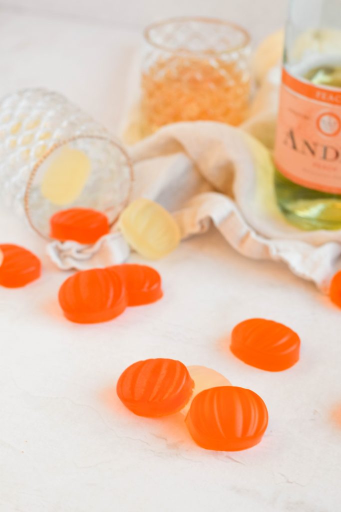 orange pumpkin shaped boozy halloween fruit snacks falling out of a glass cup with champagne bubbles around them