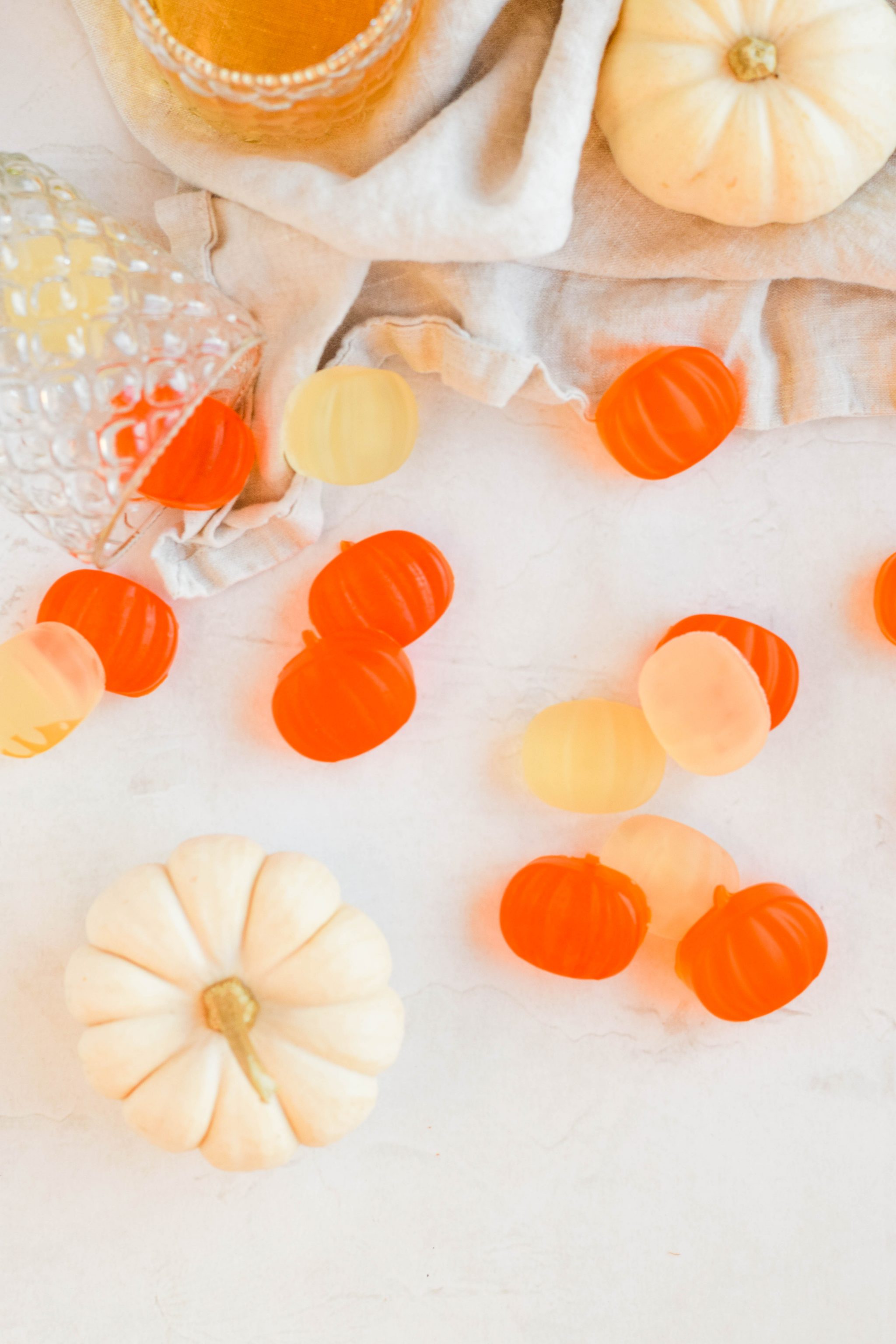 pumpkin shaped halloween jello shots spread out on white background with linen and glass in background.