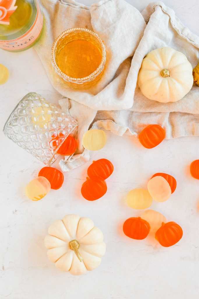 pumpkin shaped boozy halloween fruit snacks spread out with cream pumpkins on white background