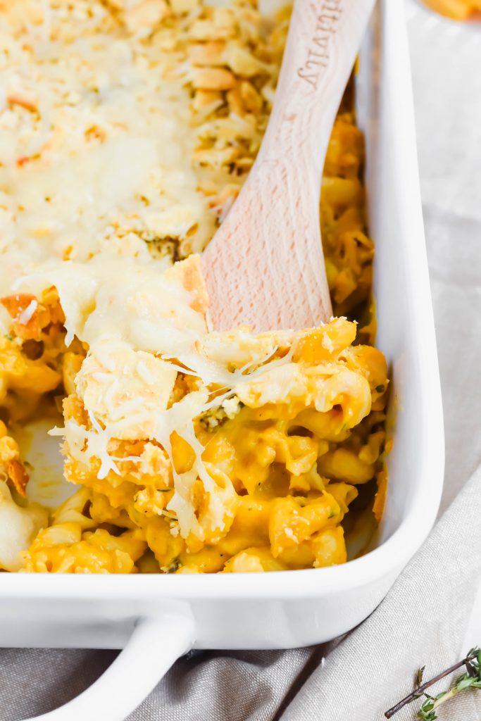 Close up of butternut squash mac in white baking dish with wooden serving spoon scooped into pasta.