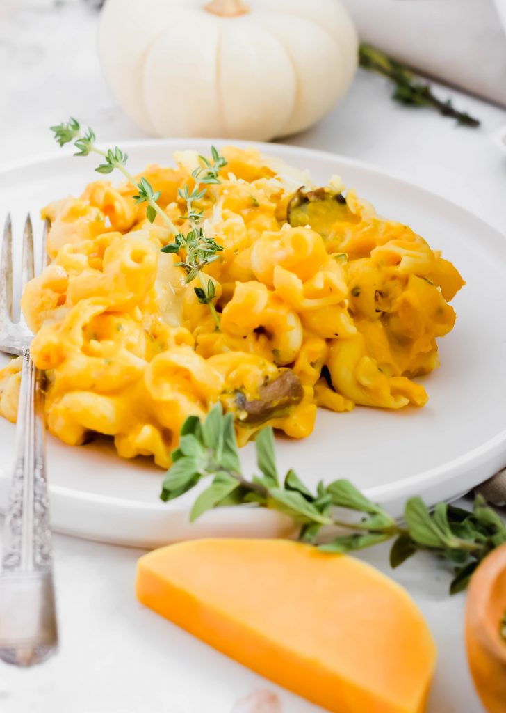 Close up shot of single serving of butternut squash mac n' cheese with fresh thyme sprig on top with fork on plate