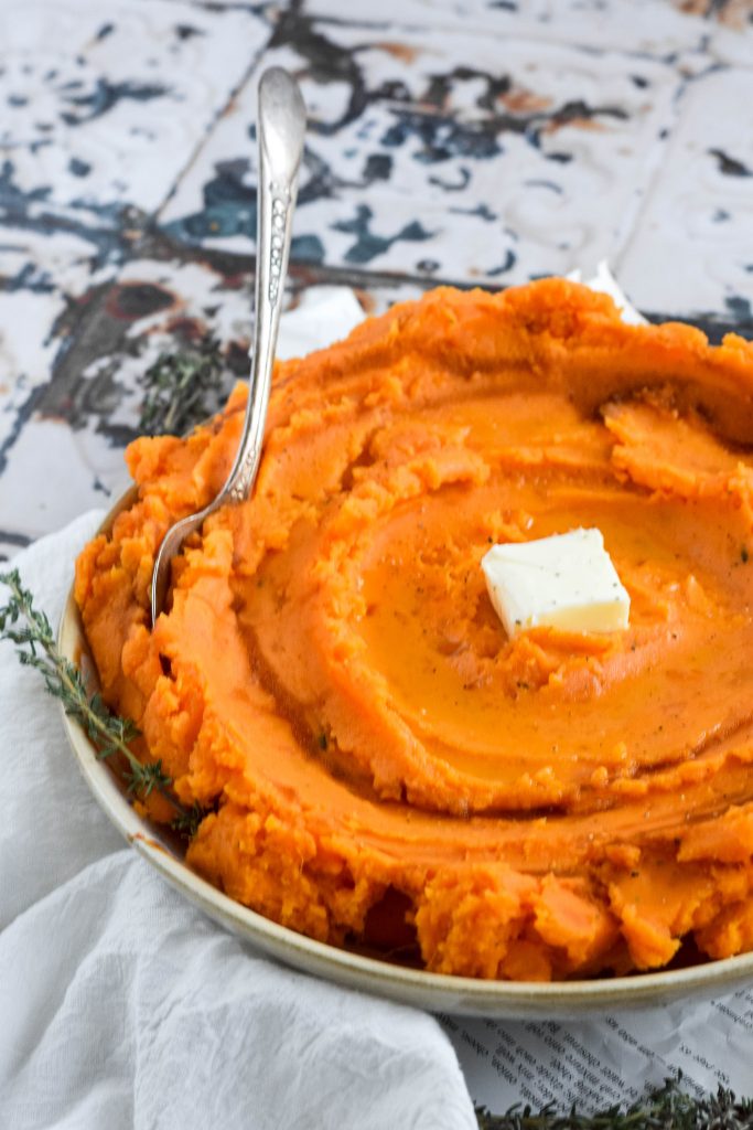 savory mashed sweet potatoes in a white bowl topped with a pat of butter on vintage background 