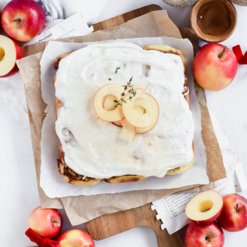 cinnamon rolls with apple pie filling topped with cream cheese frosting and apple slices on a wooden serving board with parchment paper