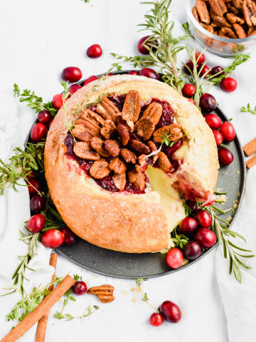 cranberry brie bread bowl filled with baked brie topped with candied pecans, cranberry sauce, and rosemary.