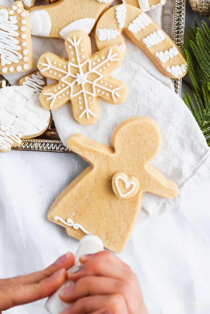 Angel shape shortbread christmas cookie being decorated with white icing on a white background with additional decorated cookies beside it