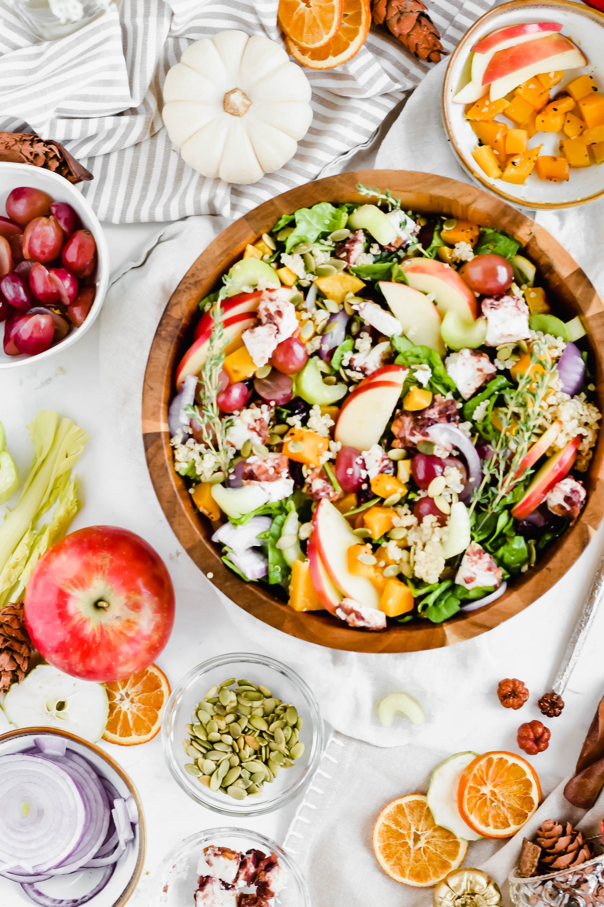 Overhead view of a Seasonal Harvest Salad filled with spinach, apples, butternut squash, grapes, and pumpkin seeds in a wooden serving bowl surrounded by salad ingredients