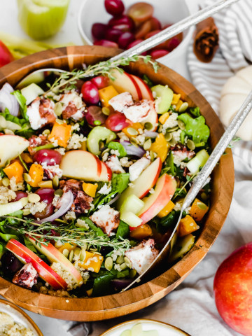 Seasonal Harvest Salad filled with spinach, apples, butternut squash, grapes, and pumpkin seeds in a wooden serving bowl with silver salad tongs