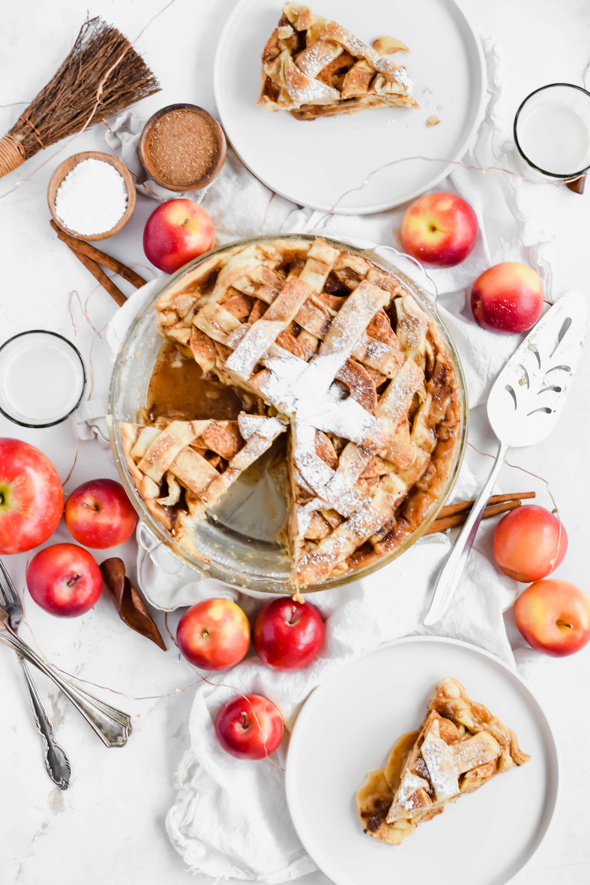 Overhead view of a simple apple pie with two slices removed and put on plates surrounded by pie ingredients