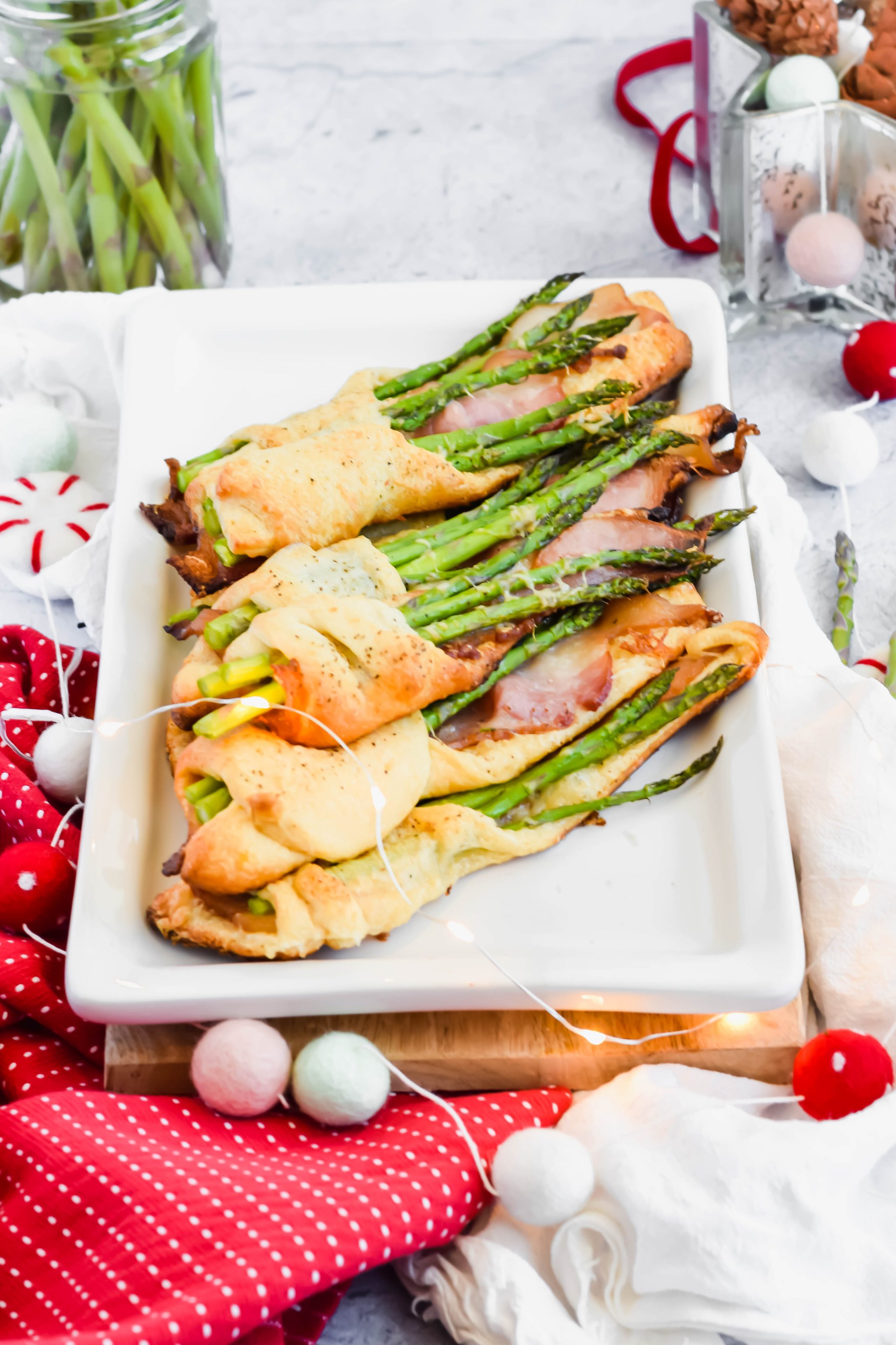 cooked asparagus and bacon pastry on white plate surrounded by Christmas decorations