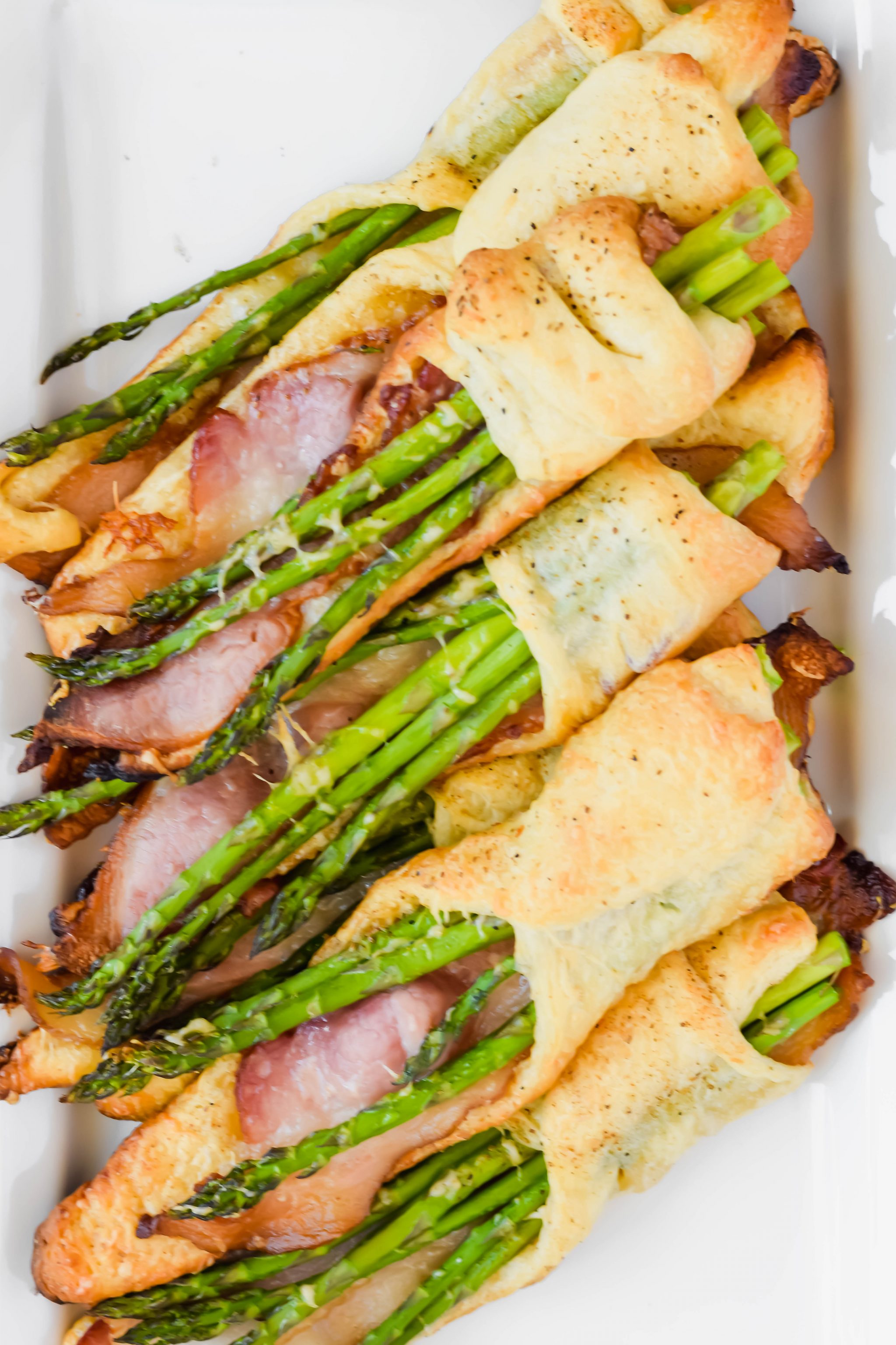 overhead shot of cooked asparagus and bacon pastry on white plate