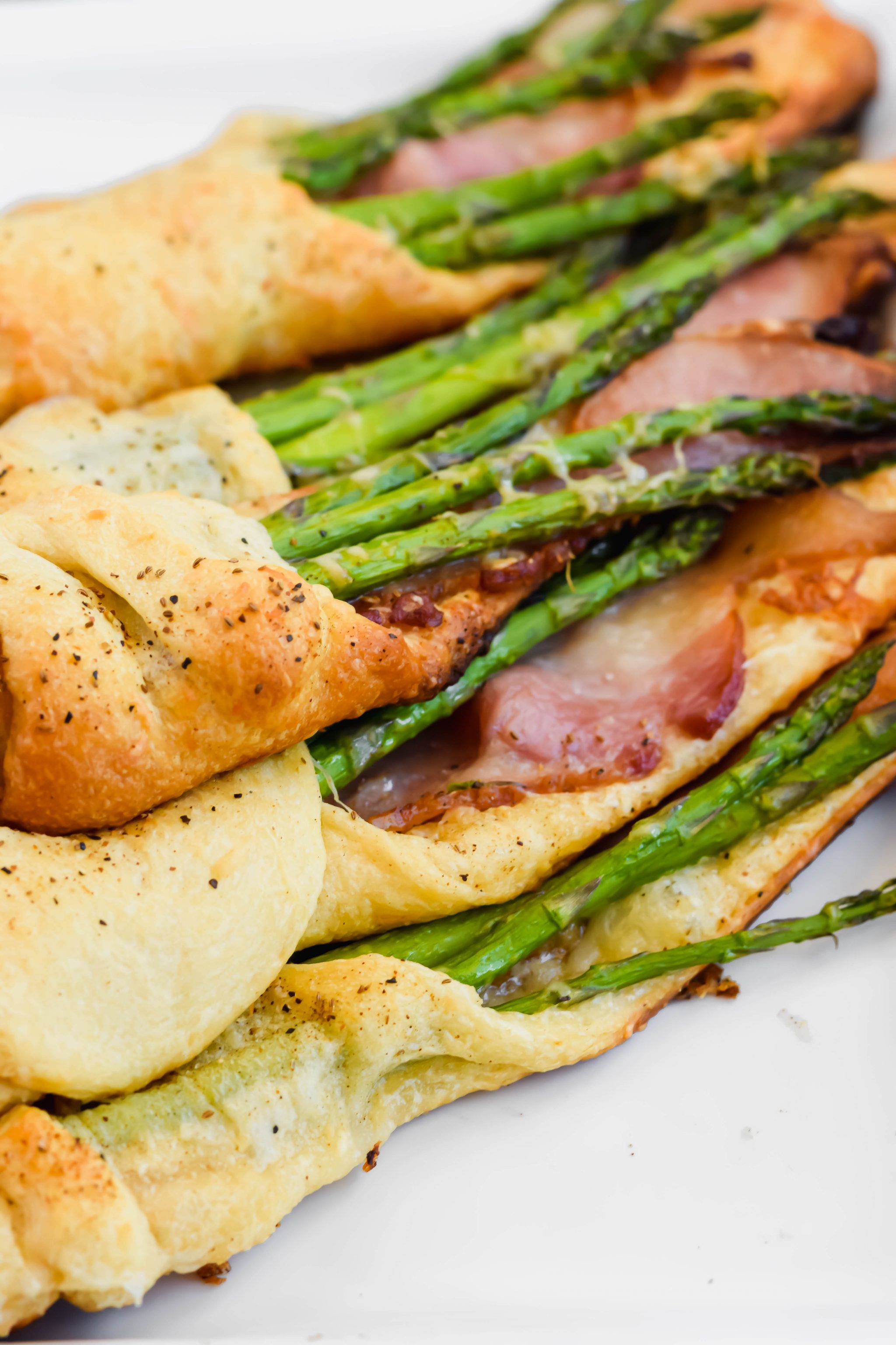 close up angled shot of cooked asparagus and bacon pastry on white plate