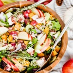 Seasonal Harvest Salad filled with spinach, apples, butternut squash, grapes, and pumpkin seeds in a wooden serving bowl with silver salad tongs