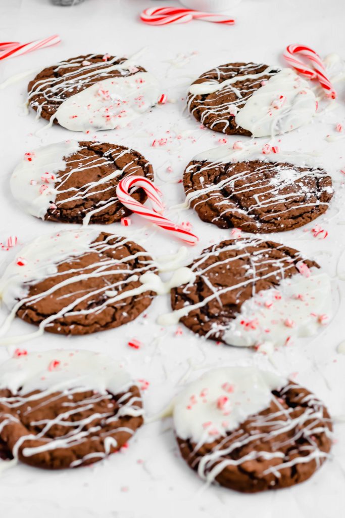Eight White Chocolate Dipped Peppermint Cookies on a white linen backdrop drizzled with more white chocolate and topped with crushed candy canes