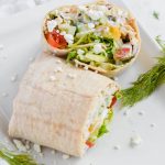 Sliced Mediterranean Chicken Wrap on a white plate sprinkled with feta cheese and fresh herbs.