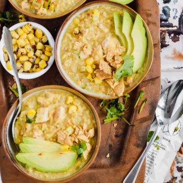Three bowls of Dutch Oven White Chicken Chili recipe on a metal serving tray surrounded by a small bowl of corn and half an avocado