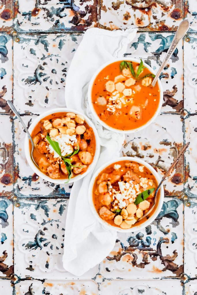 Three bowls of Spicy Sausage and Cauliflower Gnocchi Soup on white linen and a distressed floral background