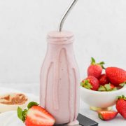 Strawberry Shortcake Smoothie in tall glass with silver straw surrounded by fresh strawberries on white background