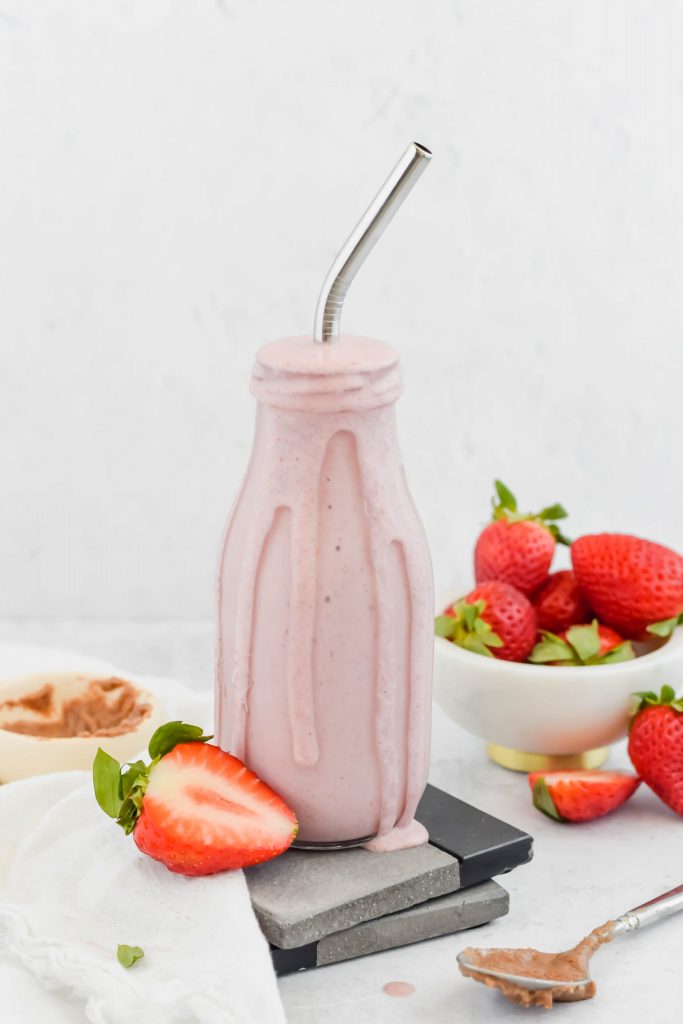 Strawberry Shortcake Smoothie in tall glass with silver straw surrounded by fresh strawberries on white background