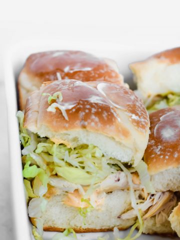 close up shot from side of Rotisserie Chicken Hawaiian Sliders in white baking with lettuce falling out of slider