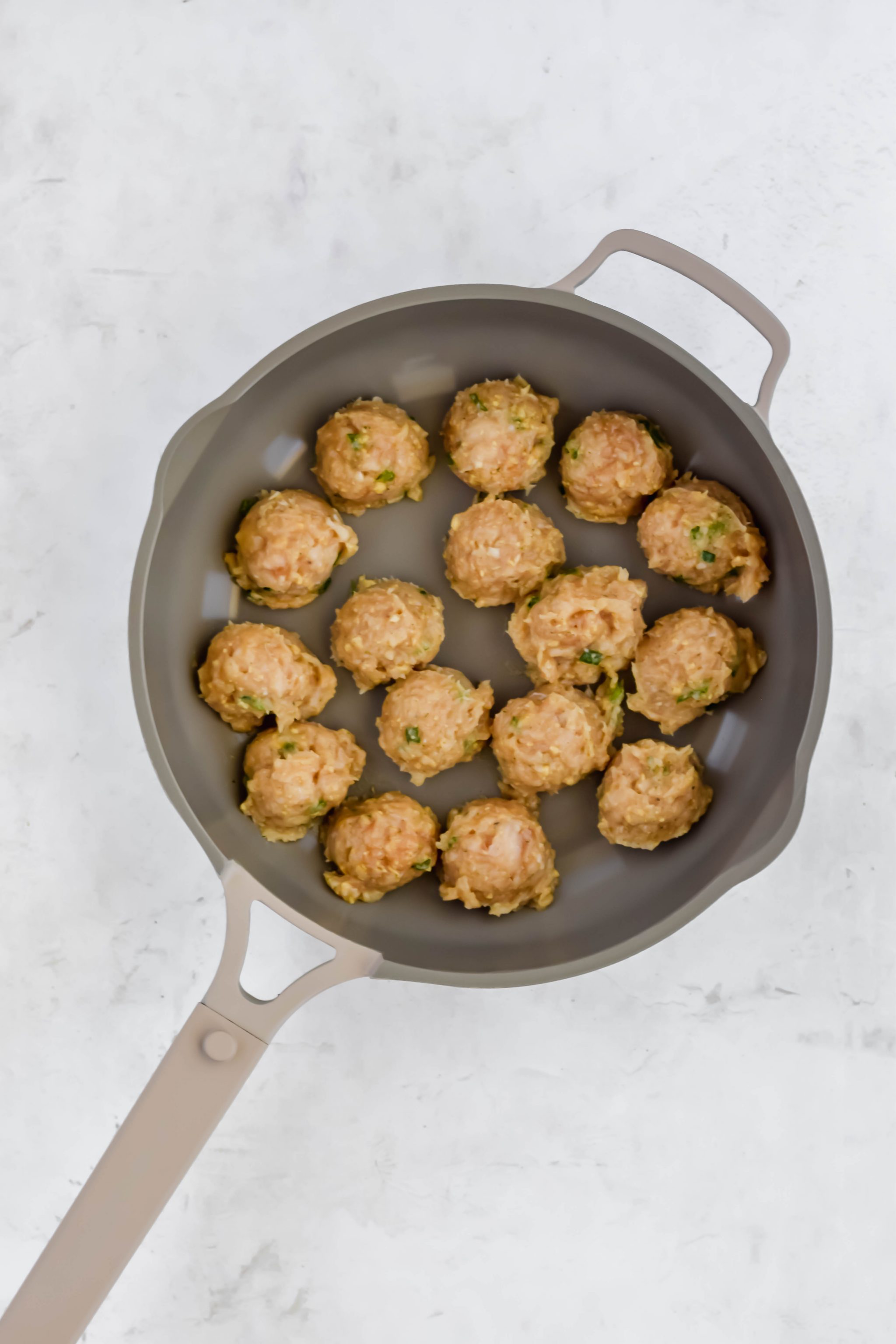uncooked Cocktail Meatballs in skillet on white background
