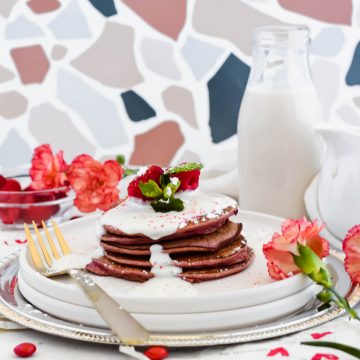 Stack of Healthy Red Velvet Protein Pancakes on a white plate topped with cream cheese frosting.