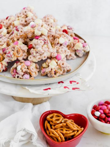 Valentine's Avalanche Cookies on white tray beside heart shaped red bowl of pretzels and small white bowl of m&m's with white background