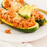 Two Ground Turkey Zucchini Boats on a white plate topped with avocado slices