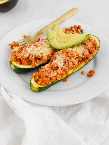 Two Ground Turkey Zucchini Boats on a white plate topped with avocado slices