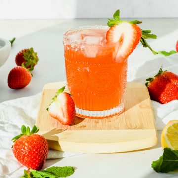 Strawberry Mint Sunshine Cocktail on a wooden cutting board surrounded my fresh strawberries, mint leaves, and half a lemon