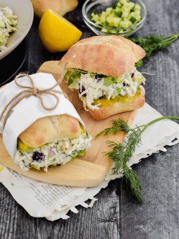 Two small sliders stuffed with Cucumber Dill Chicken Salad on a small wooden cutting board