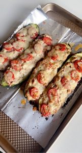 4 zucchini boats topped with cheese and tomato slices on piece of tin foil on top of baking sheet