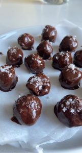 multiple peanut butter truffles covered in chocolate and topped with flakey sea salt on parchment paper with white background