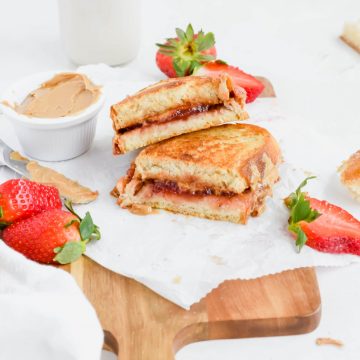 Two slices of Grilled Peanut Butter and Jelly stacked on top of each other next to a small bowl of peanut butter and fresh strawberries