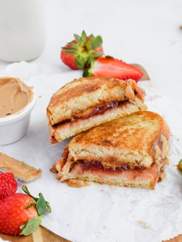Two slices of Grilled Peanut Butter and Jelly stacked on top of each other next to a small bowl of peanut butter and fresh strawberries.