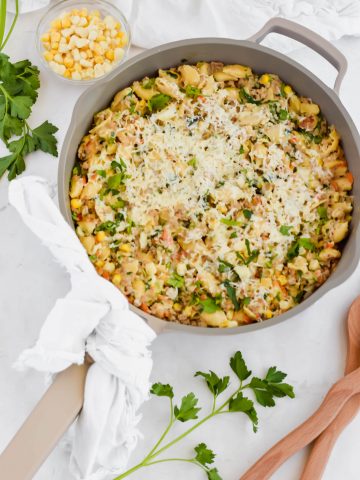 Healthy Skillet Shepherd's Pie with two wooden serving utensils, a small bowl of corn, and fresh herbs.