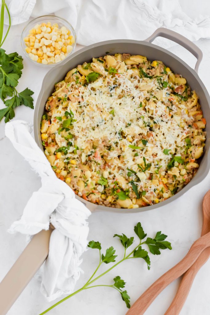 Healthy Skillet Shepherd's Pie with two wooden serving utensils, a small bowl of corn, and fresh herbs.