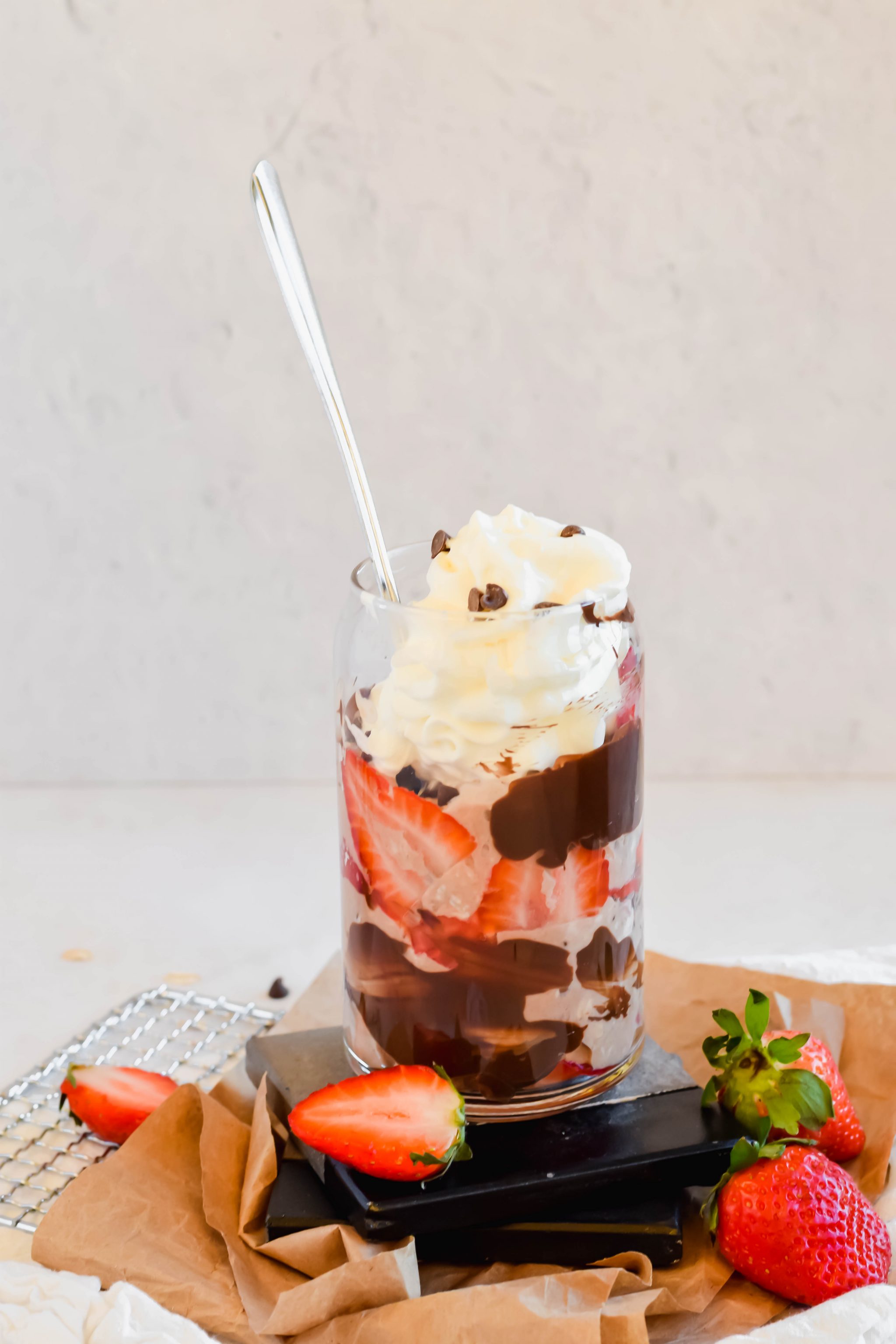 Strawberry Chocolate Brownie Overnight Oats in a tall glass topped with whipped cream surrounded by fresh strawberries