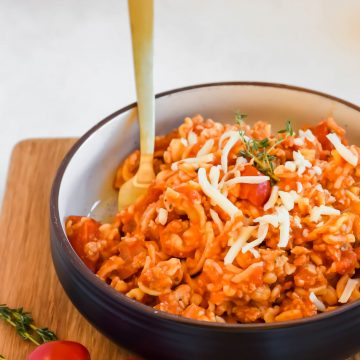 Healthy Goulash Pasta in a black serving bowl with a gold fork on a wooden cutting board