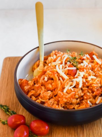 Healthy Goulash Pasta in a black serving bowl with a gold fork on a wooden cutting board.