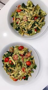 overhead shot of two bowls of pesto pasta salad on white background