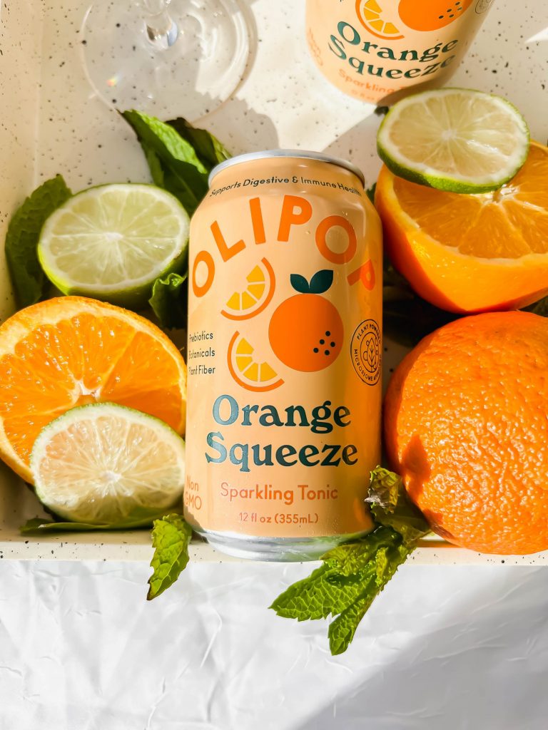orange can of OLIPOP soda surrounded by fresh oranges and limes