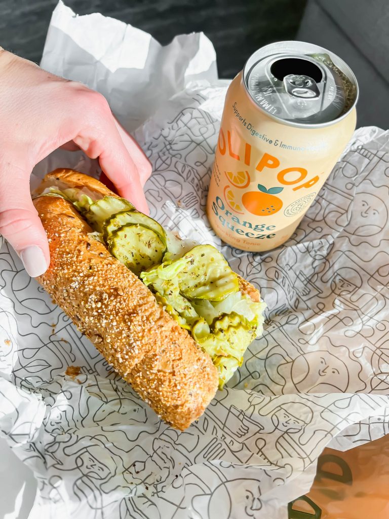 hand holding a sub sandwich with an open OLIPOP