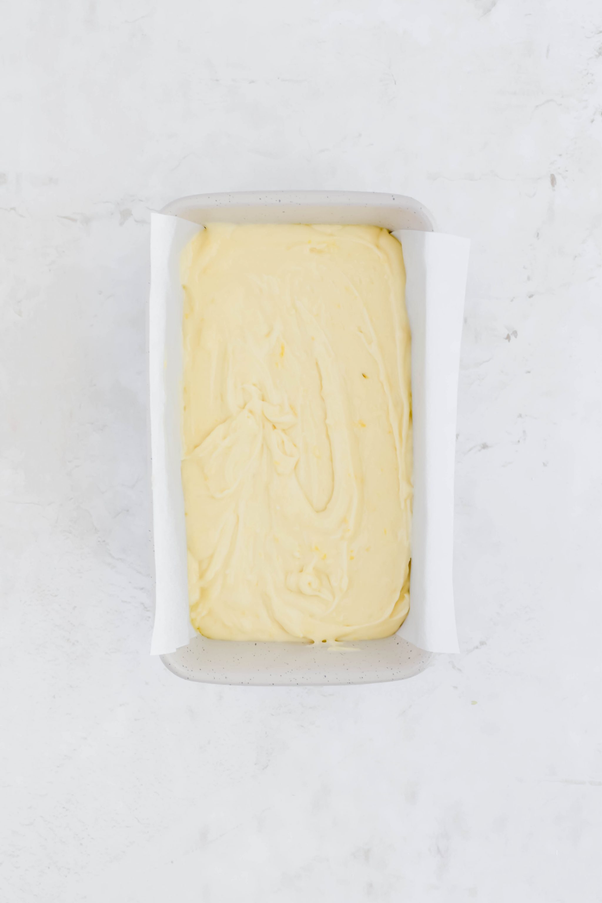 Greek yogurt lemon loaf batter in parchment lined loaf pan on white background.