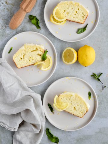 three slices of lemon quick bread on white plates garnished with lemon slices and mint leaves.