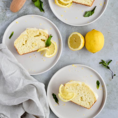 three slices of lemon quick bread on white plates garnished with lemon slices and mint leaves.