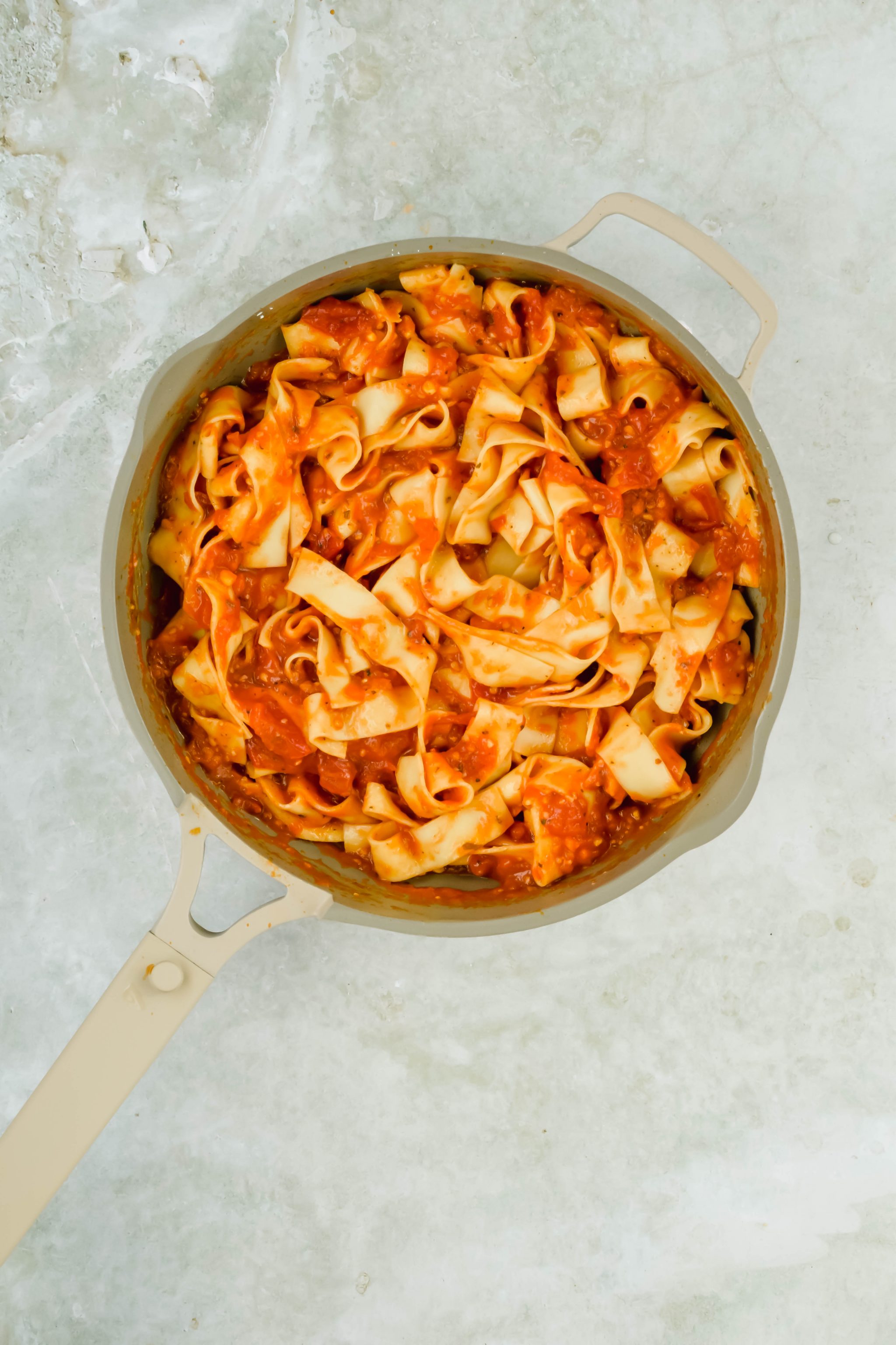 Pappardelle pasta in a sauce pot mixed with roma tomato sauce.