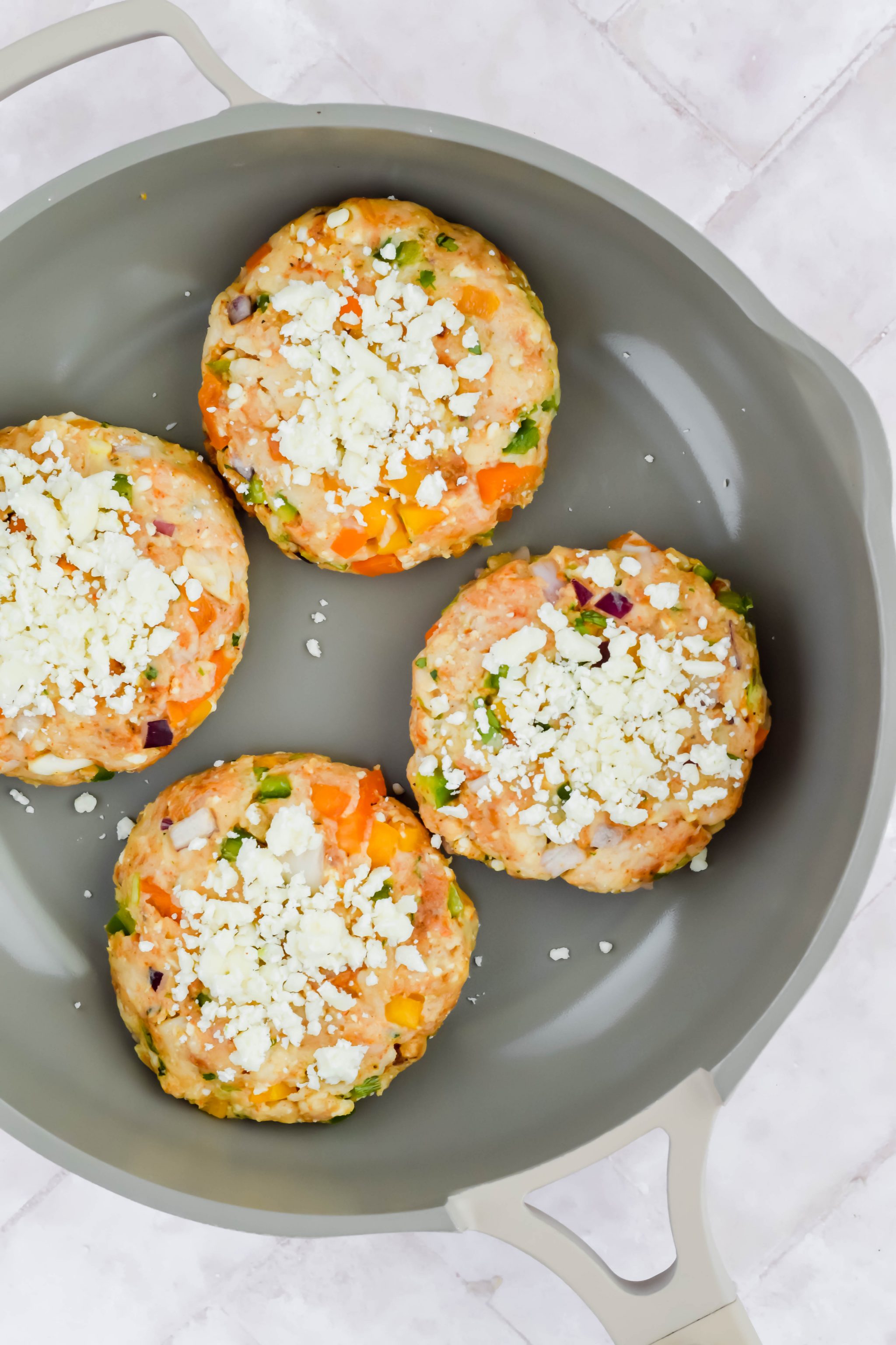 raw fajita burgers topped with cotija cheese crumbles on gray skillet.